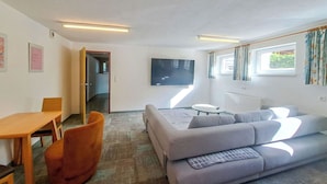 A living room with a sofa, a table, a TV, and a window with curtains. - Lovely apartment for 6 guests with WIFI, TV and terrace (Thurmbach)