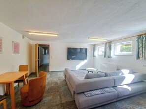 A living room with a sofa, a table, a TV, and a window with curtains.