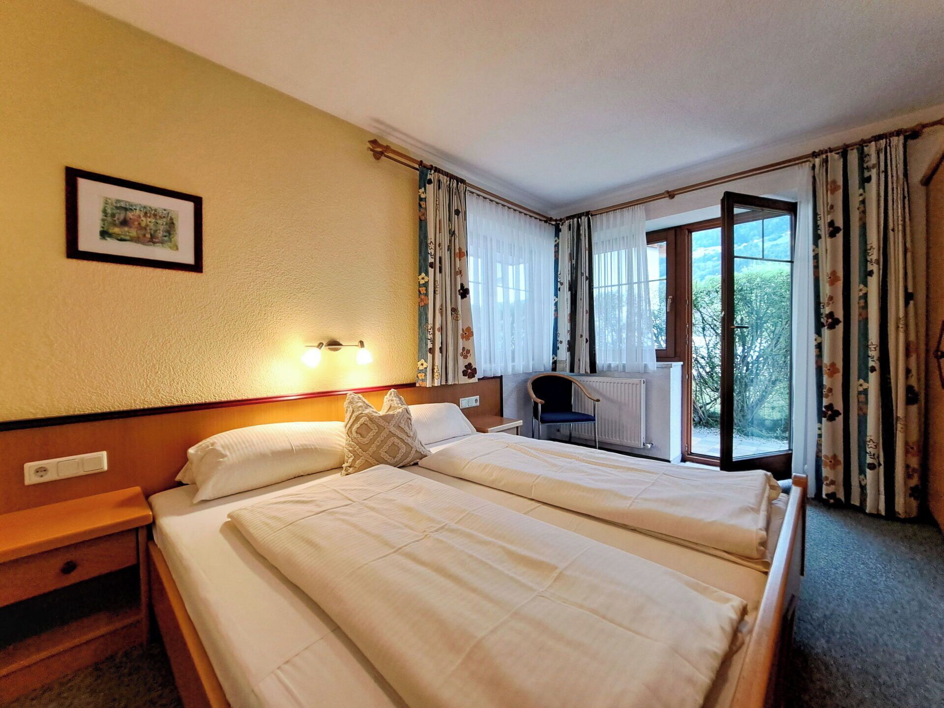 A hotel room with a double bed, bedside tables, a desk with a chair, and a window with curtains.