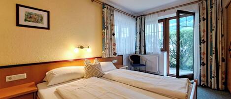 A hotel room with a double bed, bedside tables, a desk with a chair, and a window with curtains.