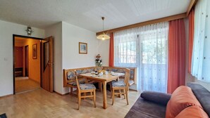 A dining area with a wooden table and chairs, a sofa, and a window with curtains. - Lovely apartment for 3 guests with WIFI, TV and balcony (Thurmbach)