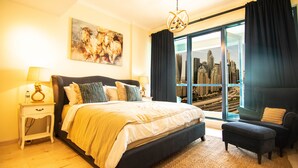 Un dormitorio con una cama grande, vista a la ciudad a través de una puerta corredera, un cuadro de paisaje urbano en la pared y vista panorámica de la ciudad por la ventana.