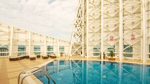 Una piscina interior con vista clara al borde, una escalera metálica y sillas de descanso.