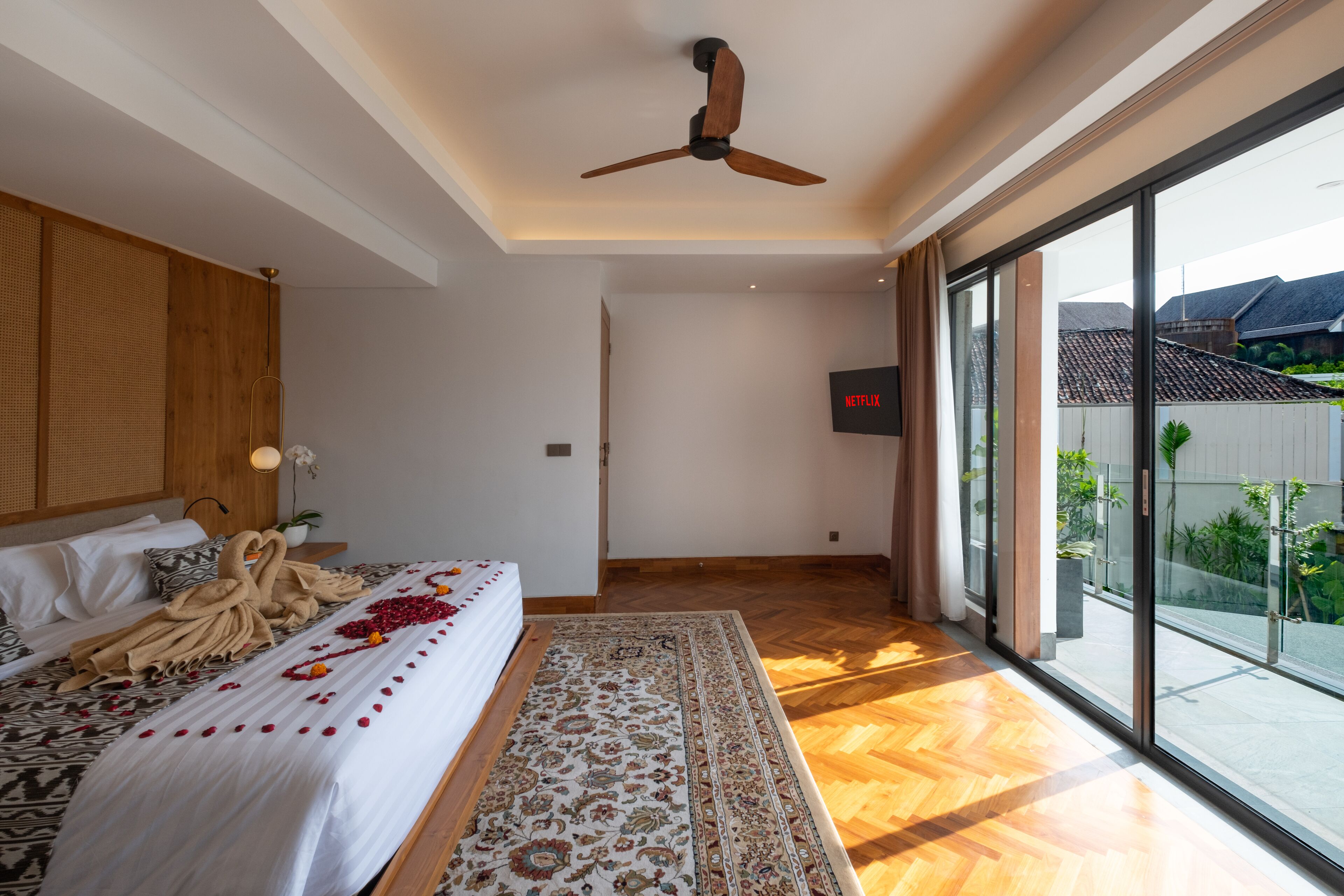 Une chambre moderne avec un grand lit, un ventilateur de plafond et une vue sur l’extérieur.