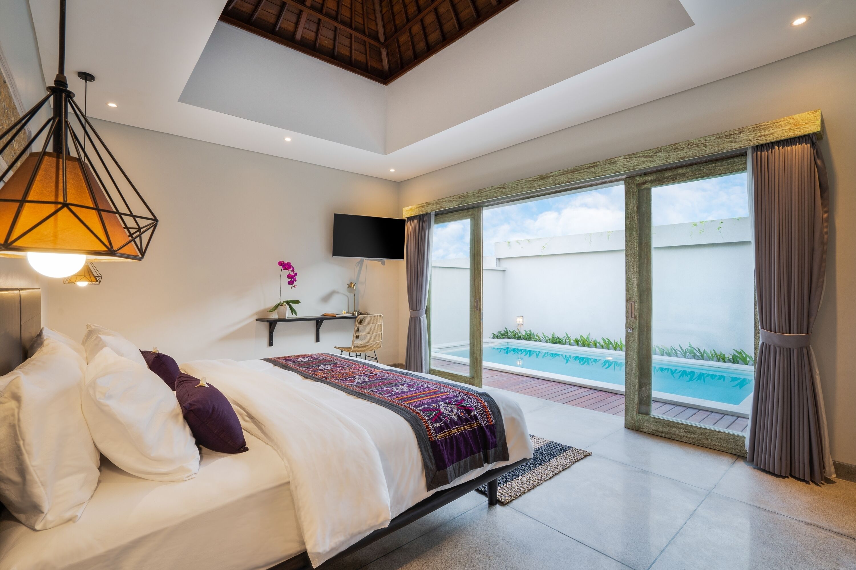 A modern bedroom with a bed, a TV, and a view of a swimming pool.