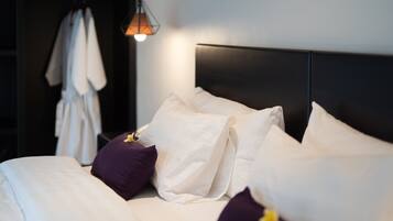 A neatly made bed with white and purple pillows, a dark headboard, and a hanging light fixture.