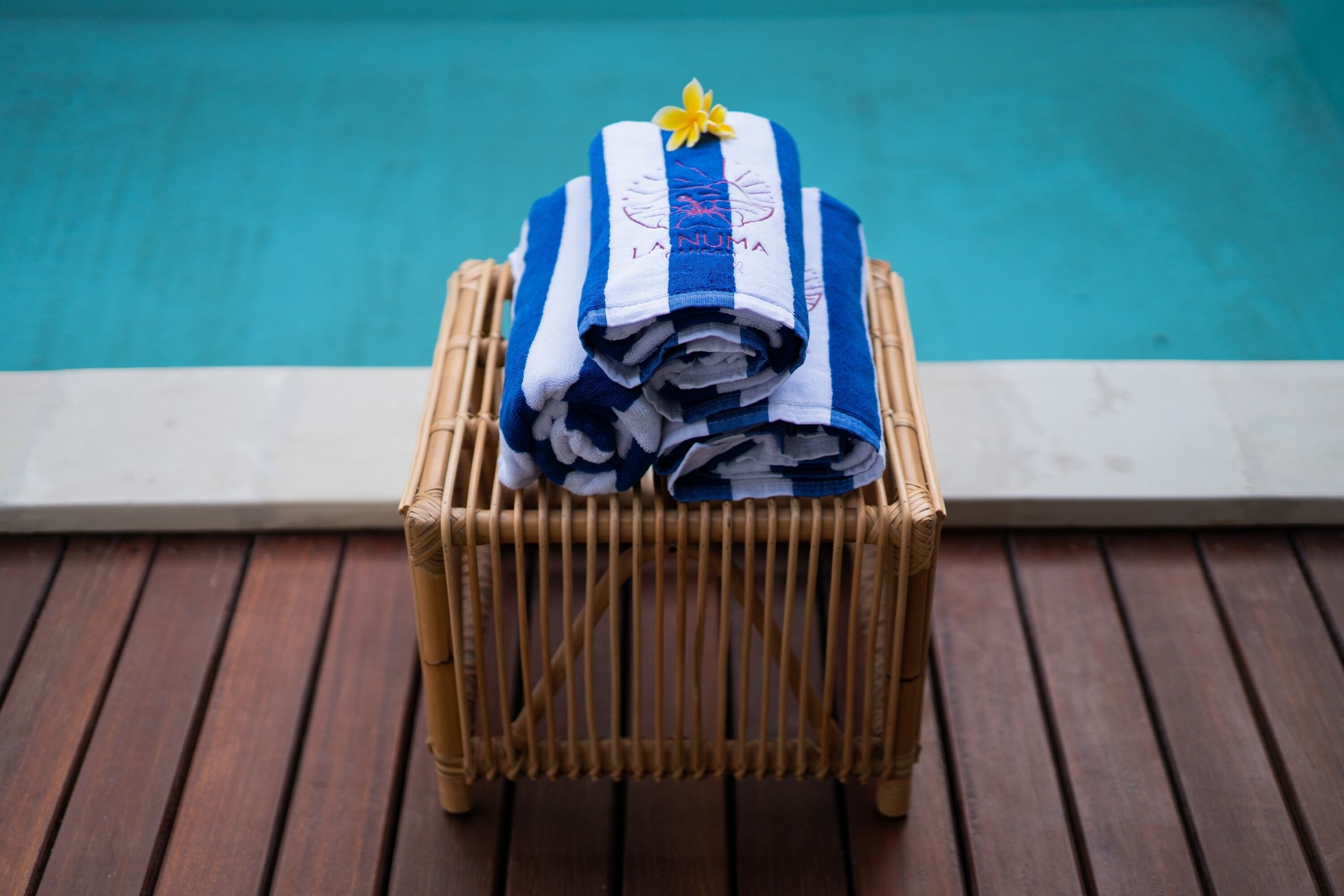 A stack of towels with a logo on a wooden chair by a pool.