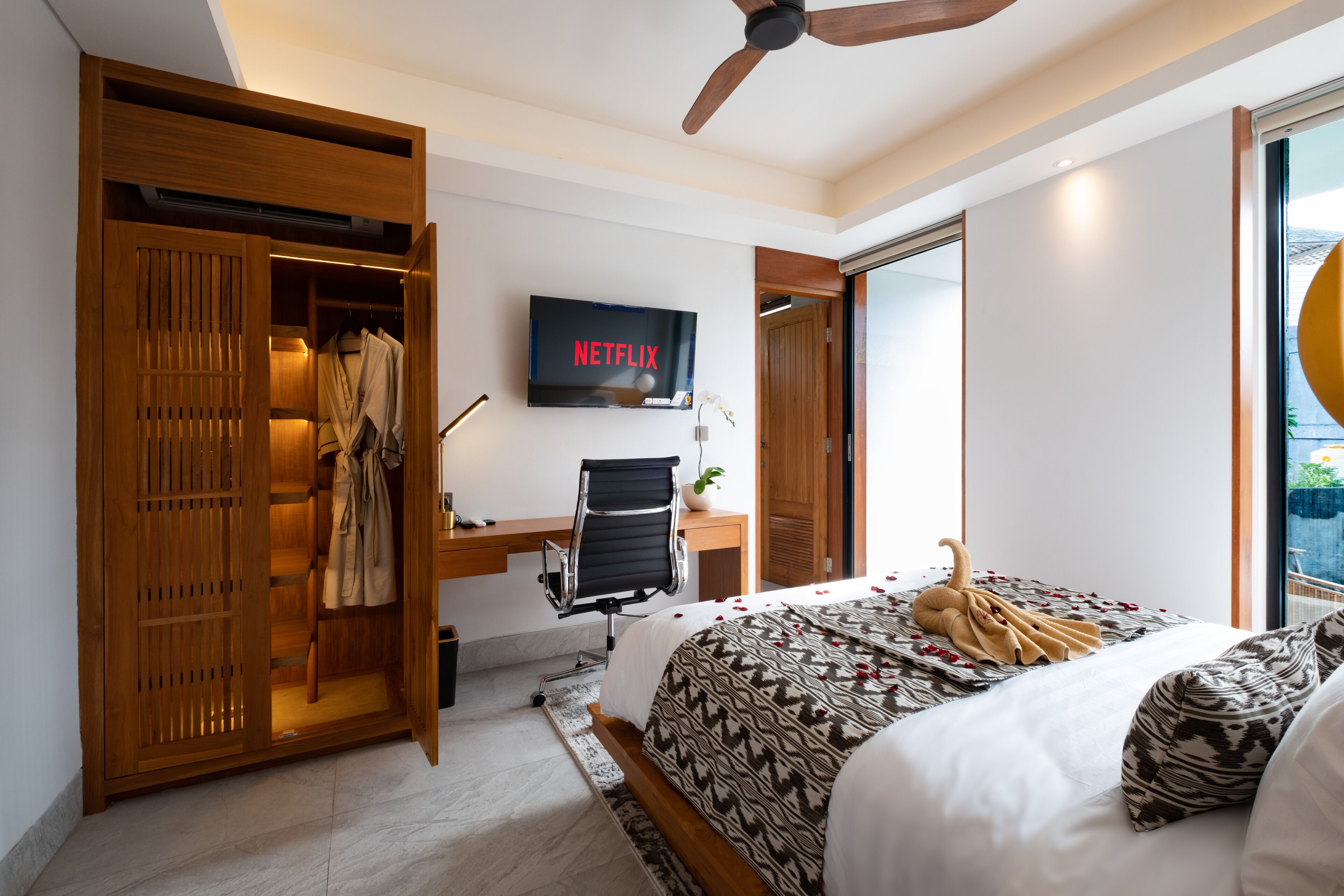 Een slaapkamer met een bed, een bureau met stoel, een kledingkast, een televisie en een plafondventilator.
