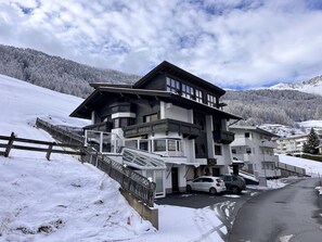 Hotel de vários andares com um teleférico, cercado por colinas cobertas de neve e céu claro.