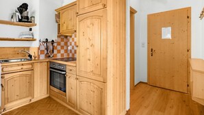 Een kleine keuken met houten kastjes, een inbouwoven en een geruit achterwand.