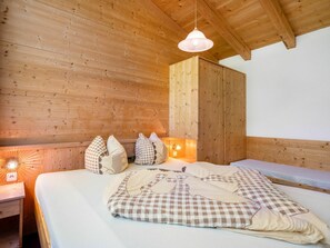 Une pièce de cabane en bois comprenant un lit, des oreillers, une table de chevet et un luminaire suspendu.
