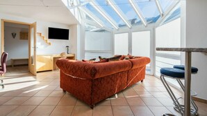 Un salon moderne avec un grand canapé, un téléviseur fixé au mur et une lucarne au plafond.