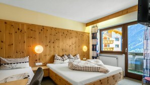 A wooden room with a bed, a desk, and a chair. There are two wall-mounted lamps and a window with a view of buildings. - Cosy apartment for 6 people with WIFI, TV and balcony (Solden)