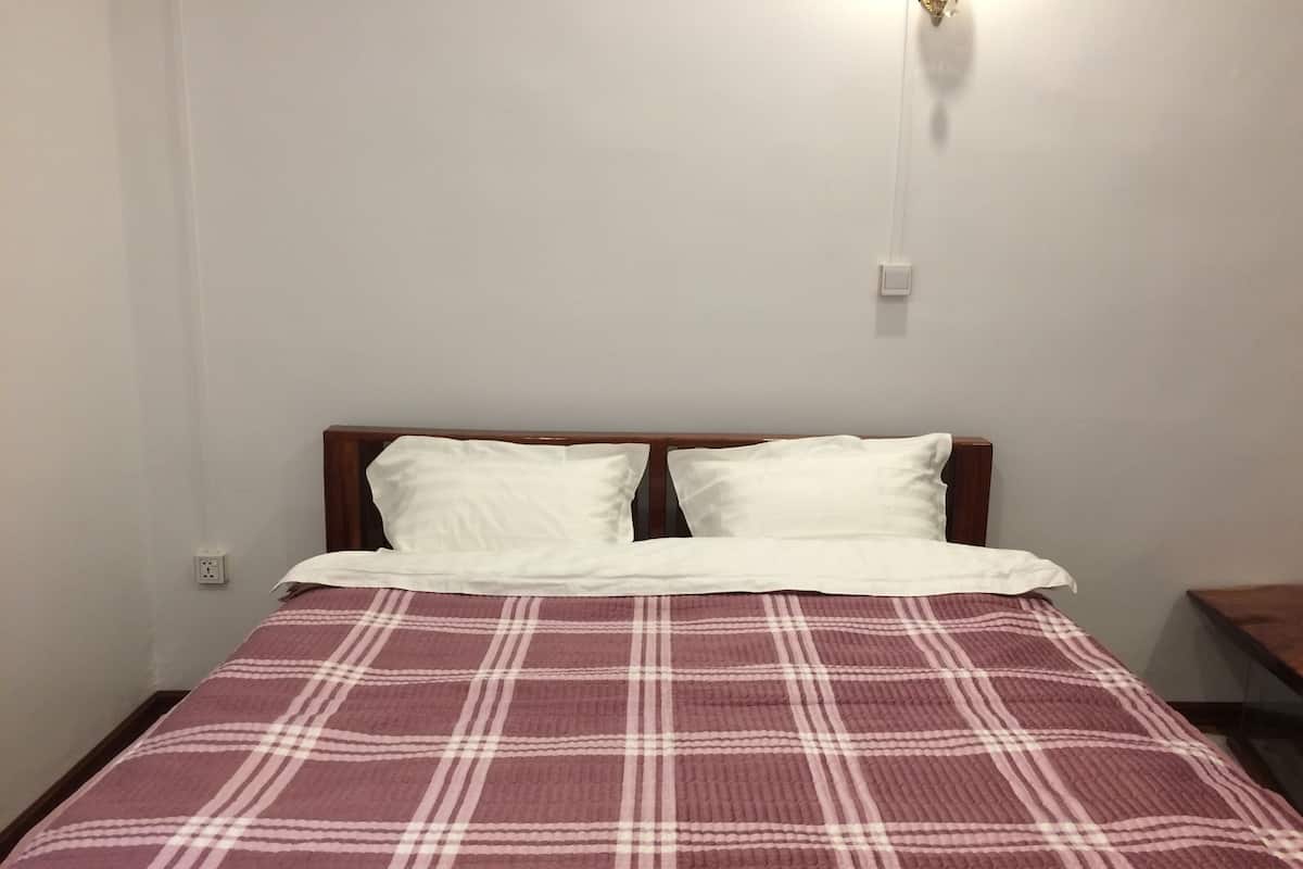 Un lit avec une couvre-lit à carreaux, une tête de lit en bois et un luminaire fixé au mur.