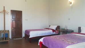 Ein Zimmer mit zwei Betten, einer Holztür, einem kleinen Tisch mit einer Lampe und einem Kleiderständer.