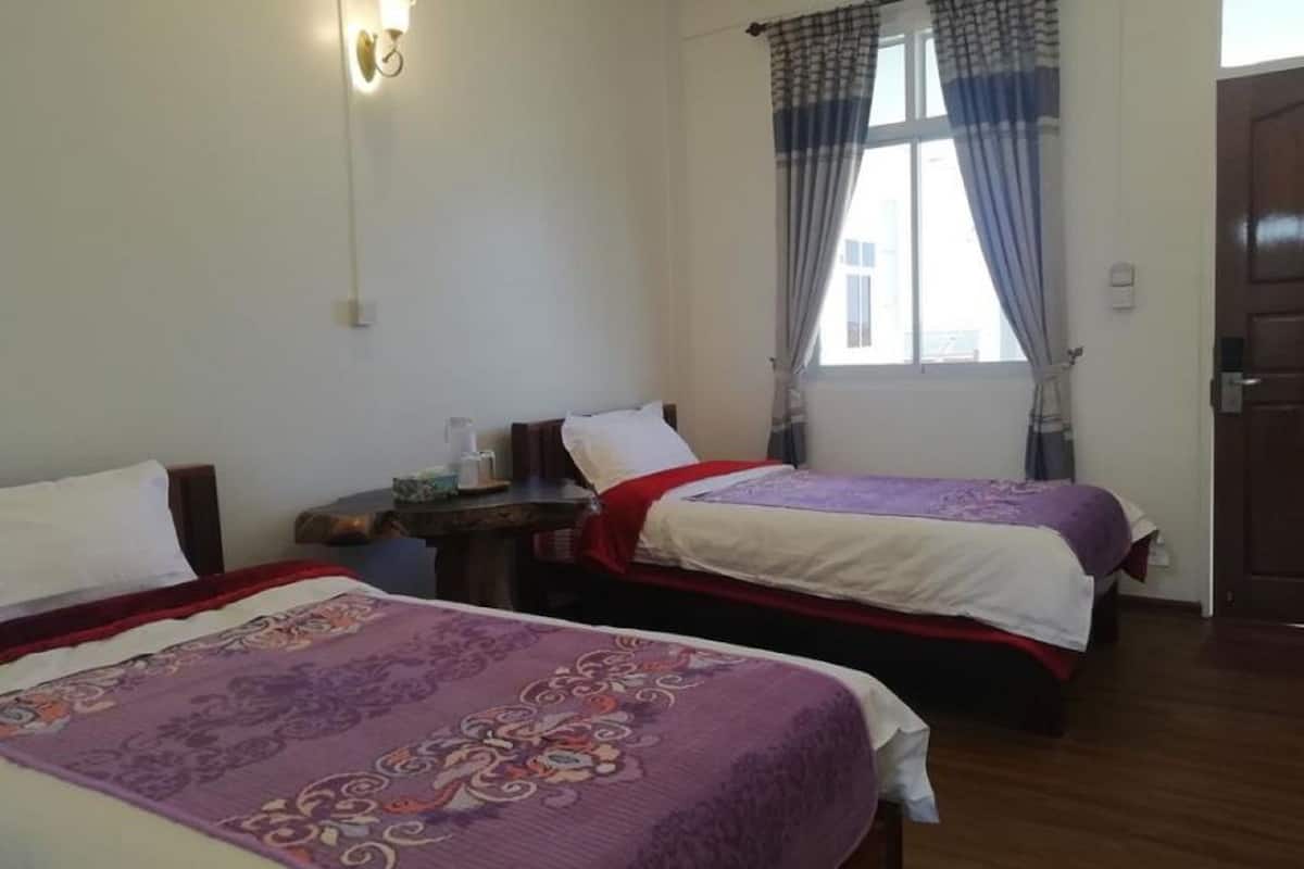 Une chambre avec deux lits, chacun recouvert d’une couvre-lit à motifs, une table de chevet avec une lampe et une fenêtre avec des rideaux.