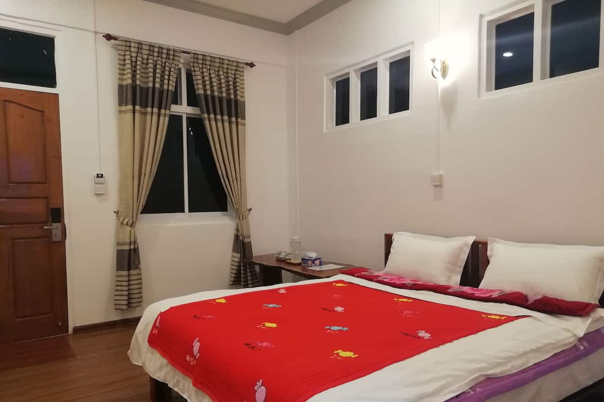 Une chambre à coucher comprenant un lit, une table de chevet, une fenêtre avec des rideaux, une porte et un luminaire fixé au mur.