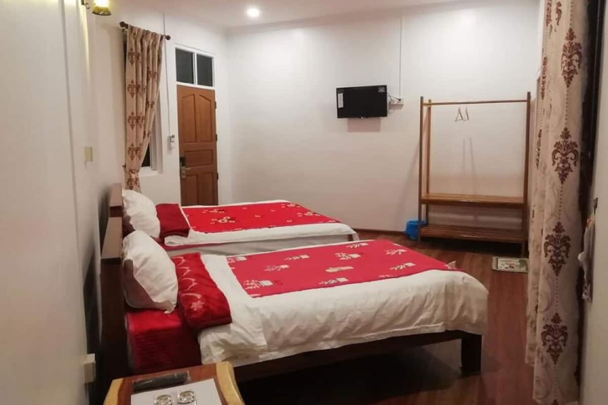 Une chambre avec deux lits, un plancher en bois, un téléviseur fixé au mur et une armoire en bois.