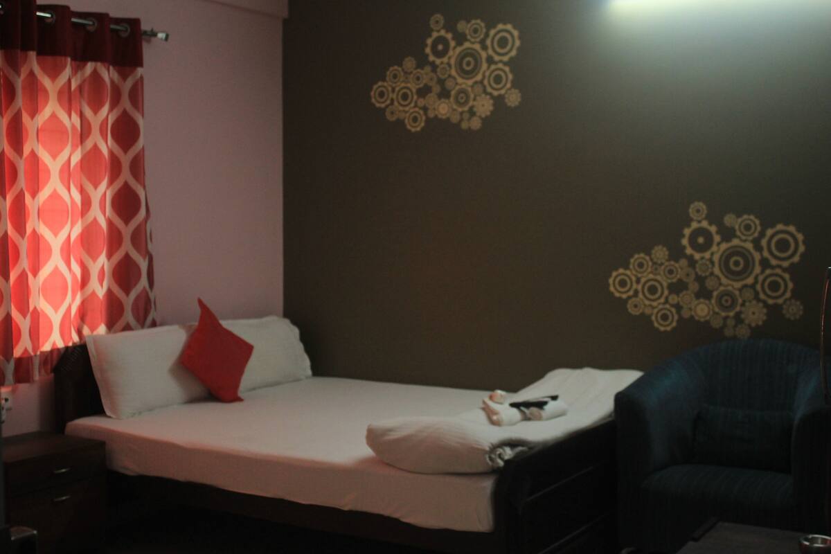 A hotel room with a bed, a red pillow, a nightstand, and a wall with circular patterns.