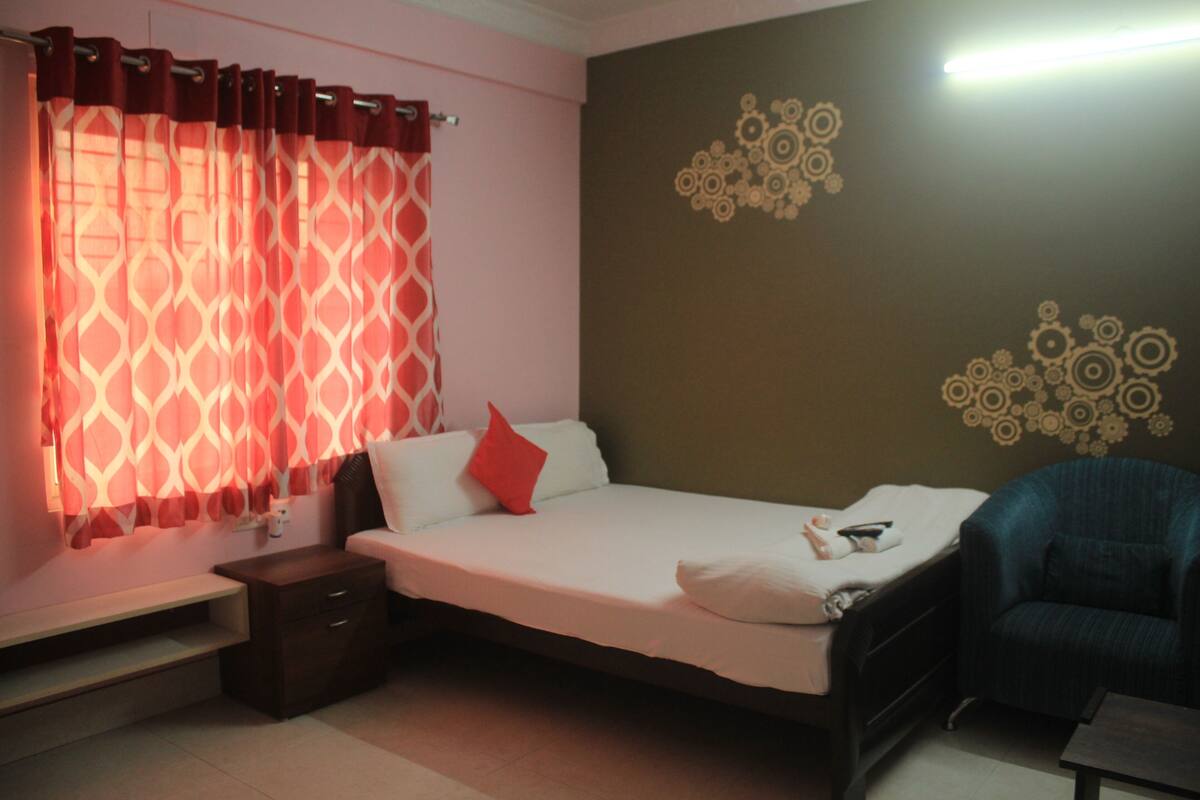 A bedroom with a bed, a nightstand, a chair, and a wall with decorative patterns.