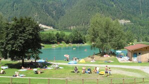 A lakeside resort with grassy areas, umbrellas, and a wooden building. - Beautiful apartment for 2 people with WIFI, TV and balcony (Fendels)