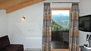 Een woonkamer met een bank, een glazen salontafel, een televisie en een balkon met gordijnen.