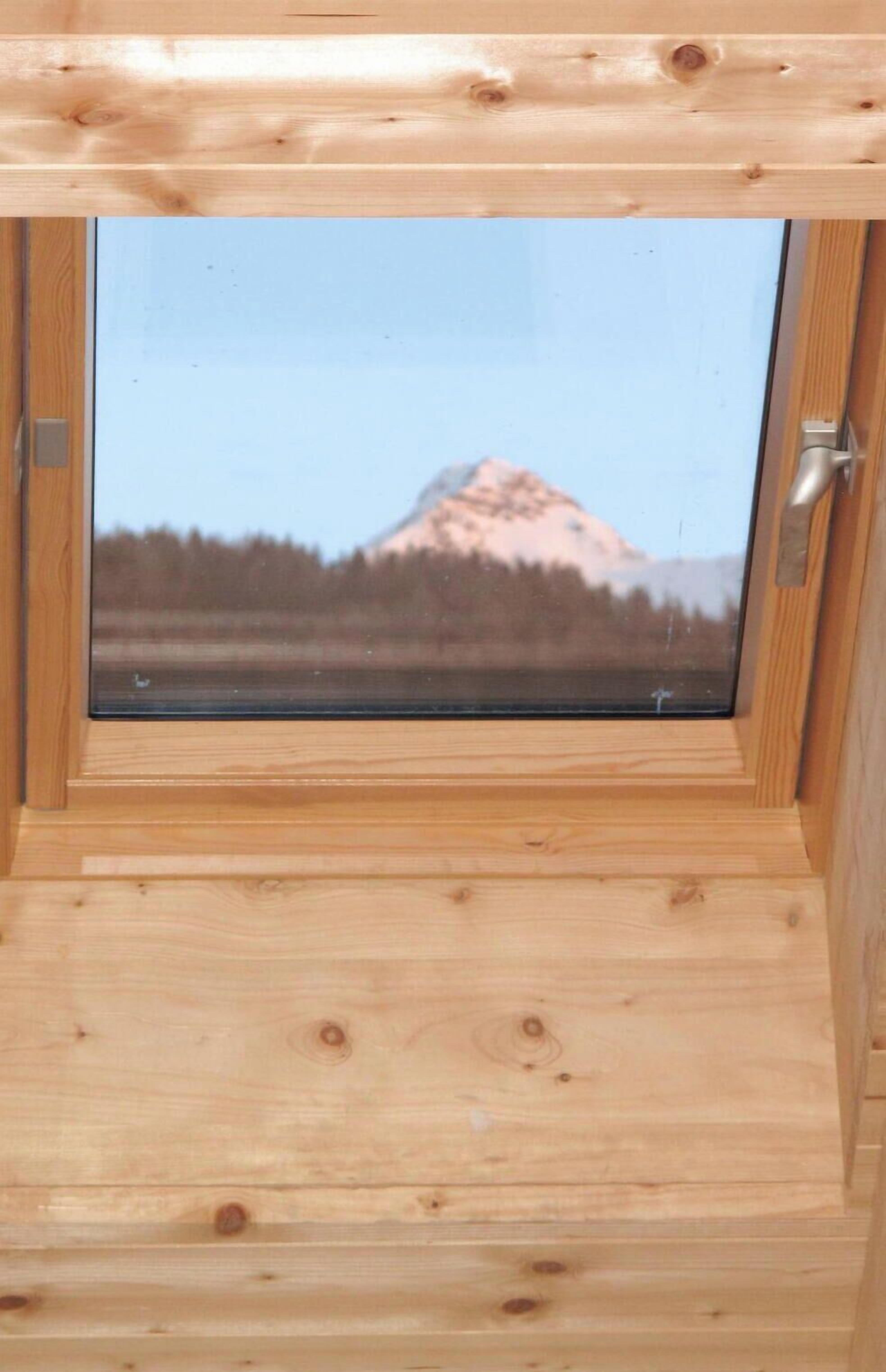 A wooden cabin with a window offering a view of a mountain.