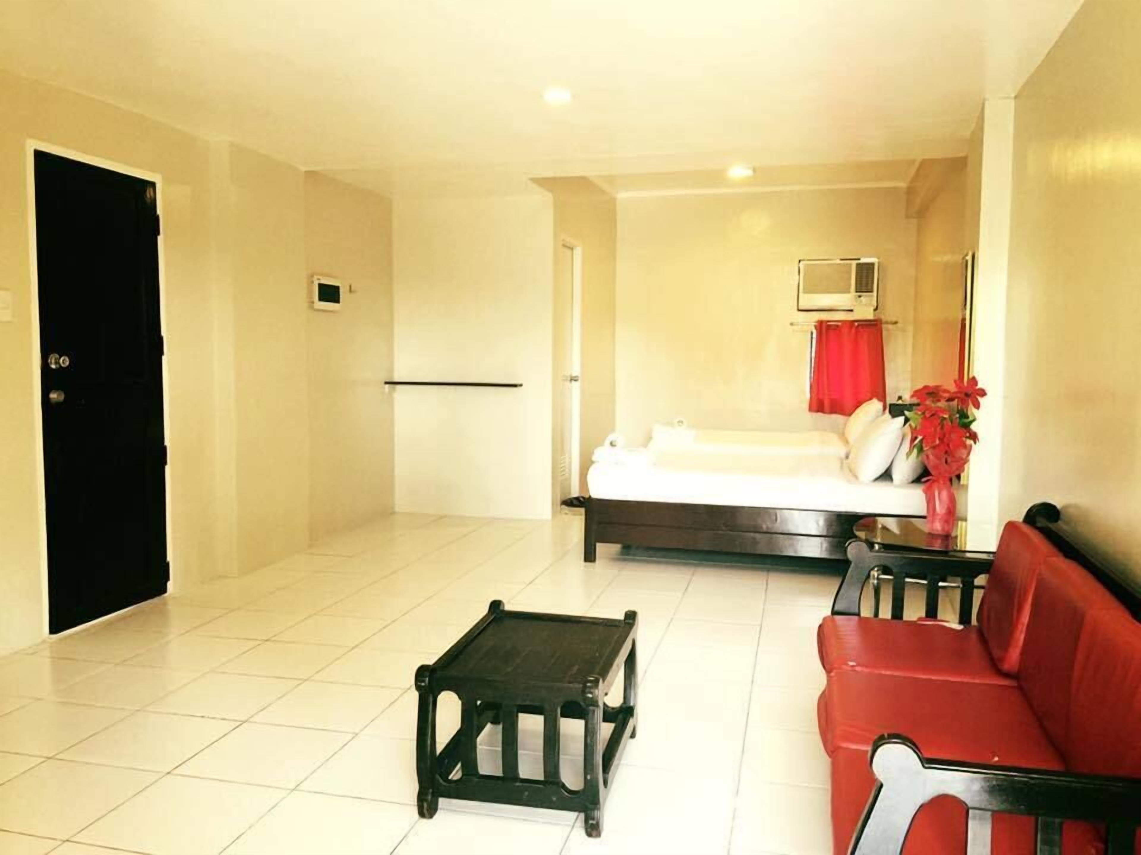 A hotel room with a bed, a red sofa, a small table, and a TV on the wall.