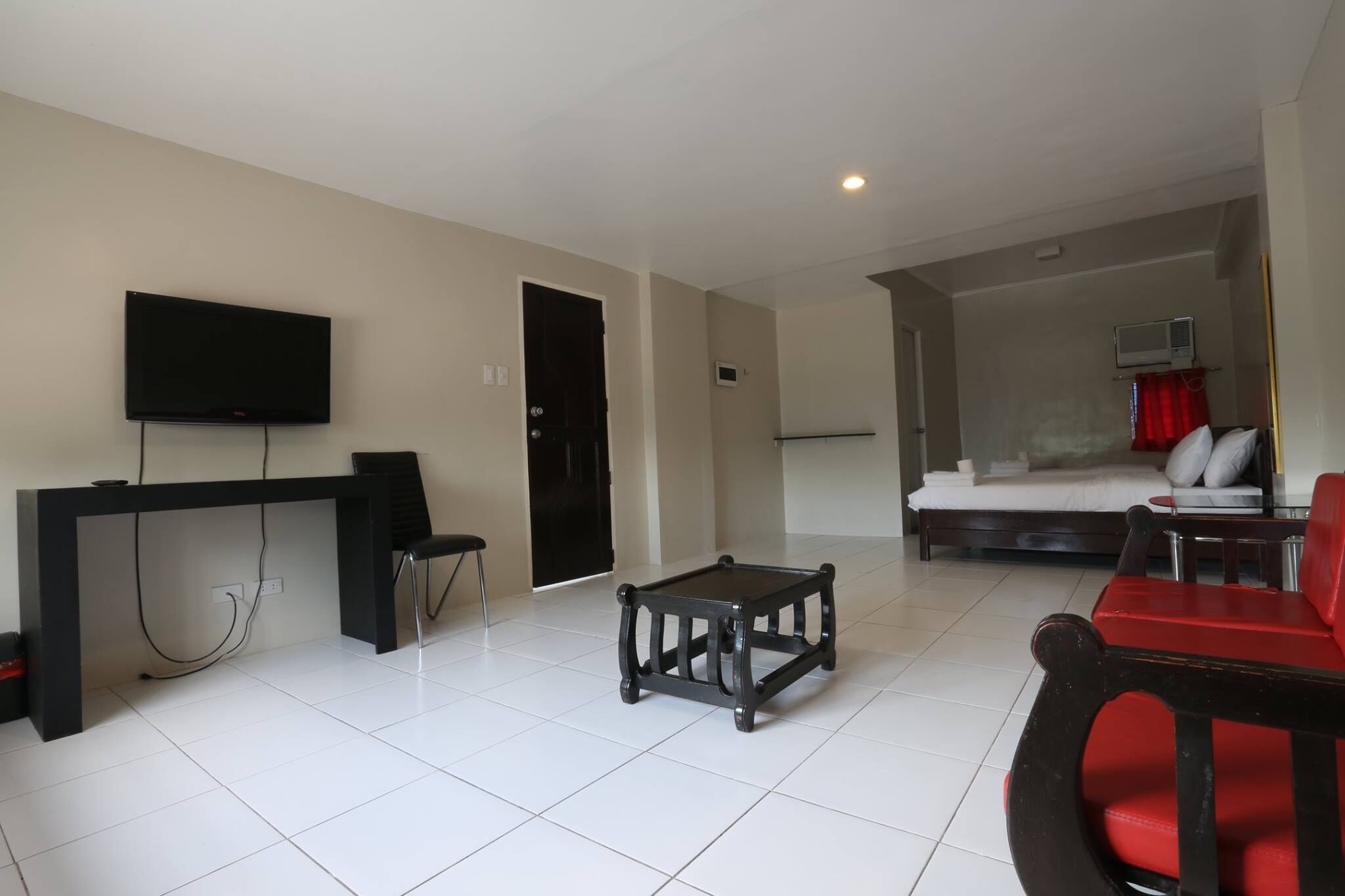 A modern living room with a flat-screen TV, a small coffee table, a sofa, and a red chair.