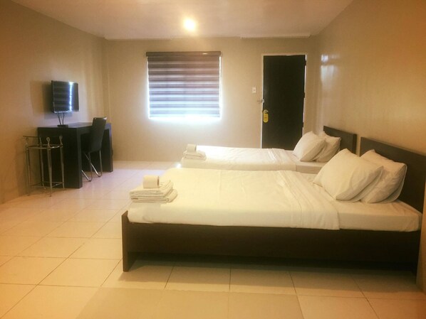 A hotel room with two beds, a TV, a desk, and a window with blinds. - Kingsville Hotel (Cauayan)