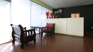 Una habitación con una mesa y sillas de madera, un mostrador de recepción y un ventanal con persianas.