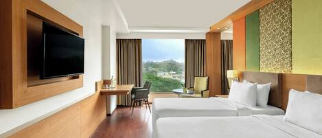 A hotel room with two beds, a desk, a chair, a TV, and a view of the city.