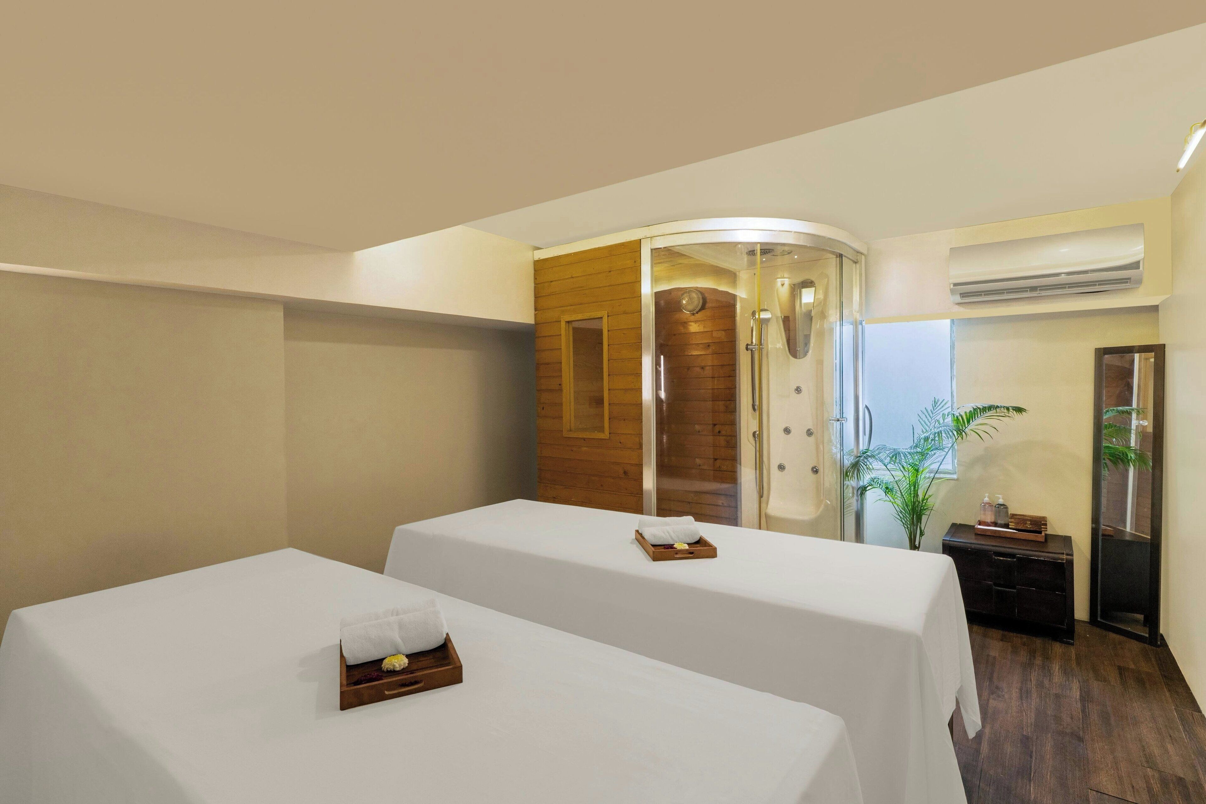 A hotel room with two beds, a wooden panel wall, an air conditioning unit, and a small plant.
