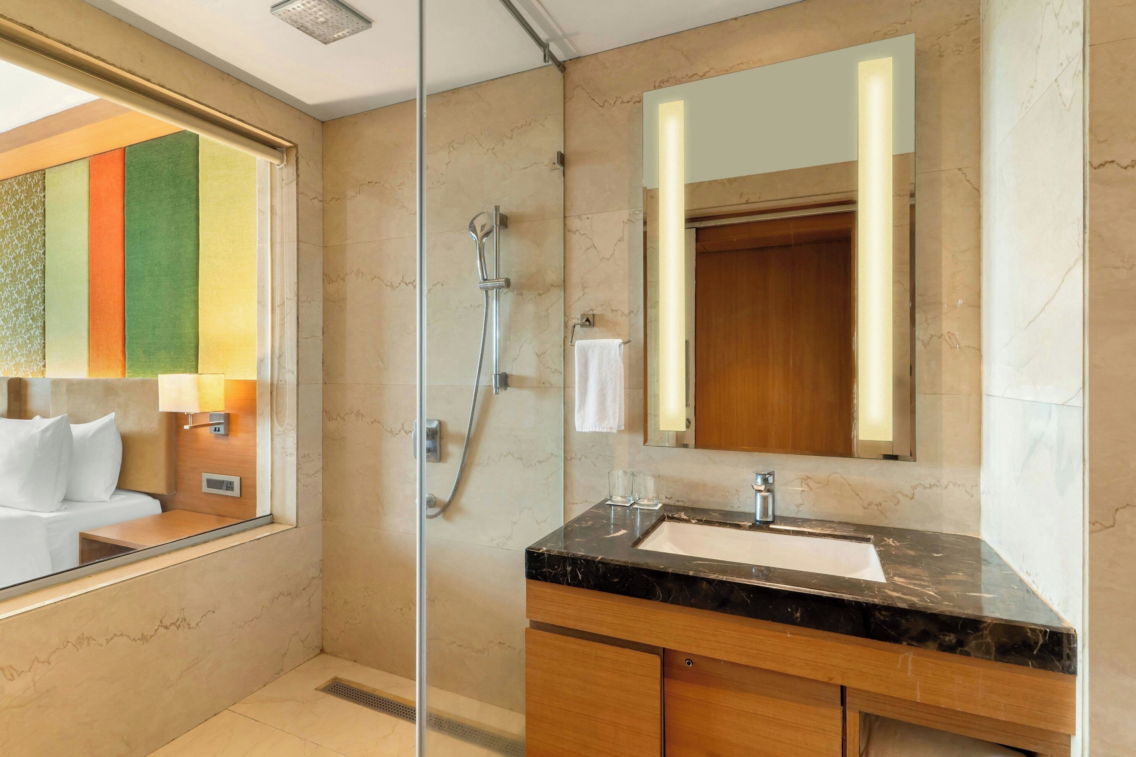 Un baño moderno con ducha de vidrio, lavamanos de mármol y un espejo grande.