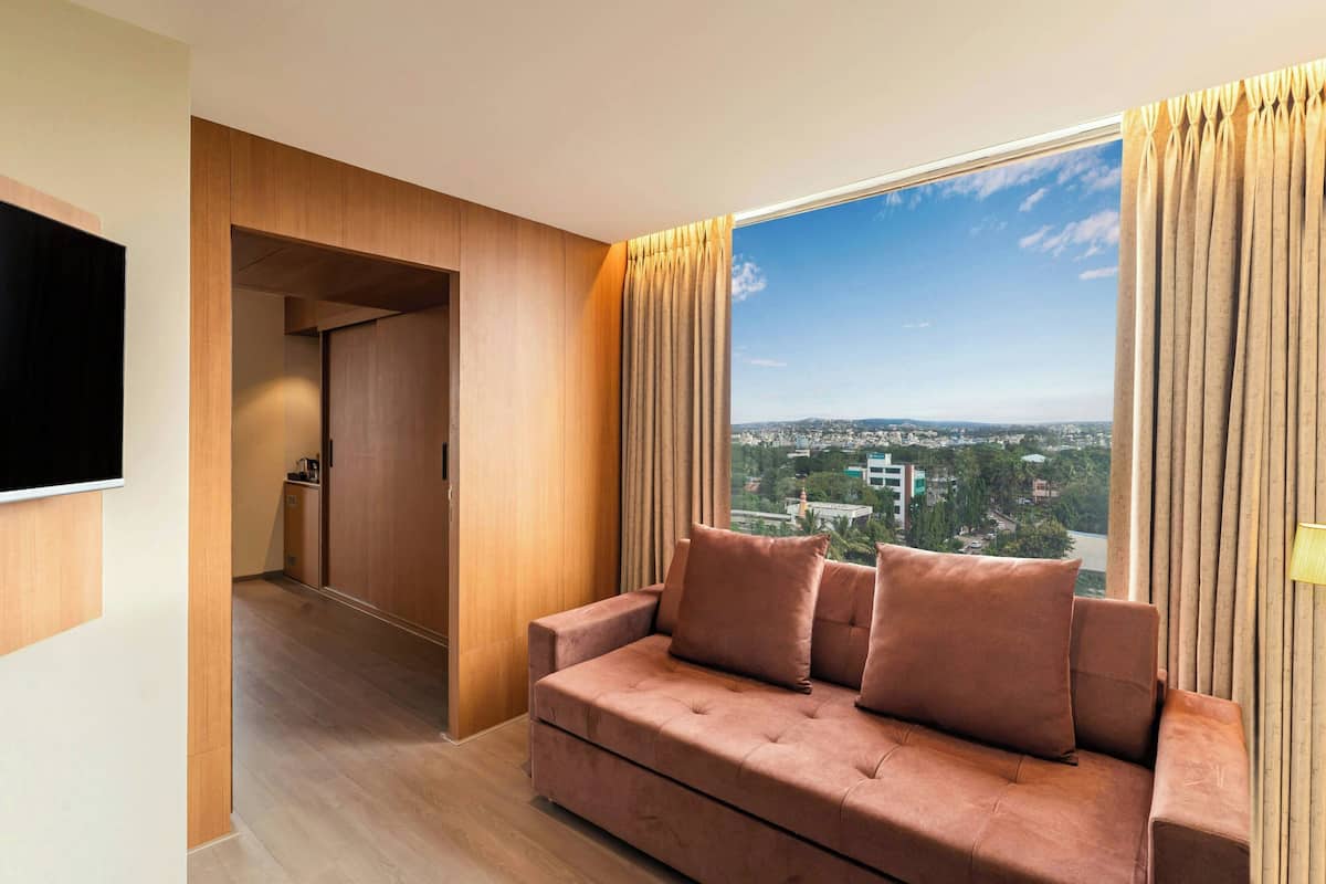 A modern living room with a sofa, a flat-screen TV, and a large window with curtains.