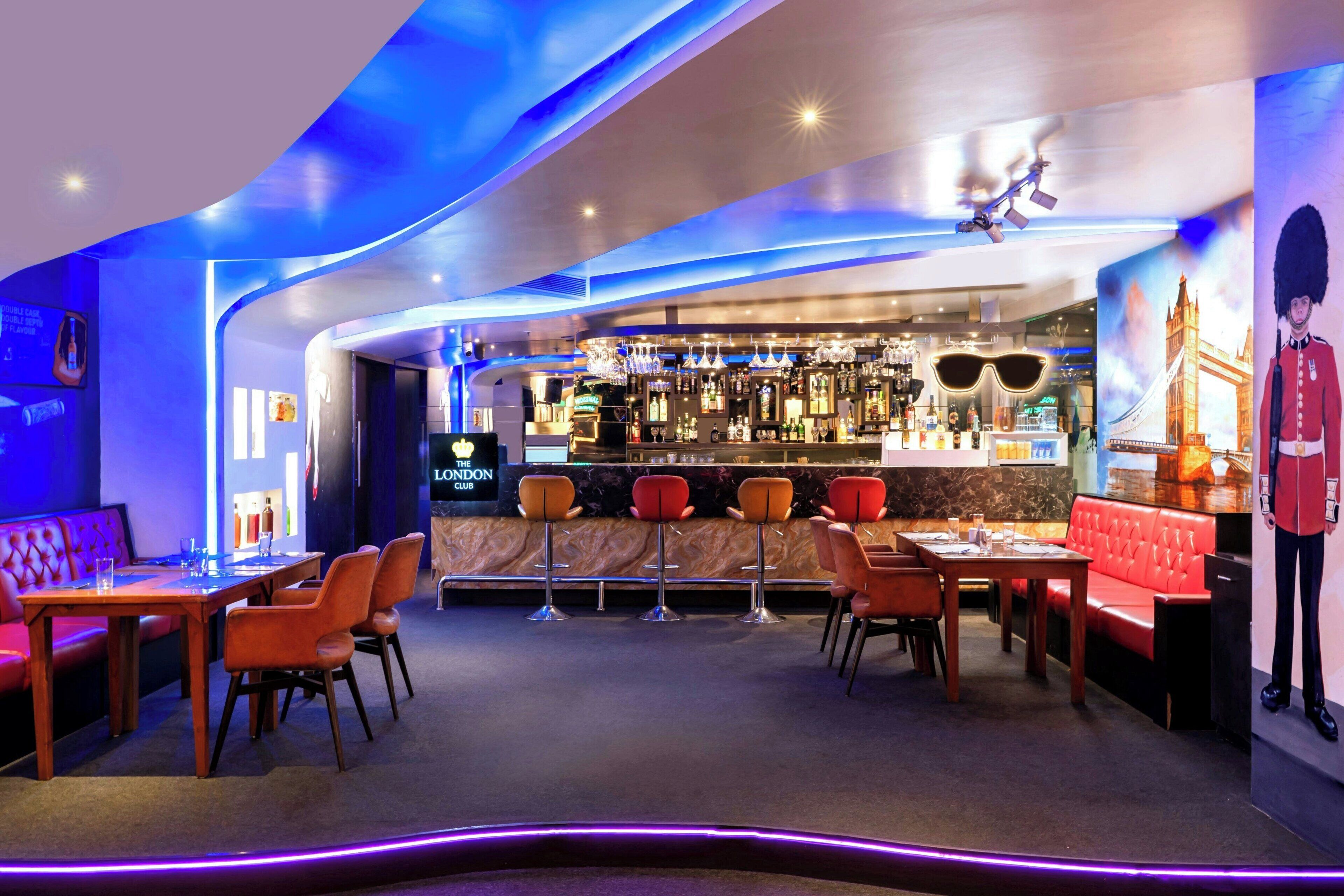 A bar area with a London-themed mural, red seating, and a variety of bottles on shelves.