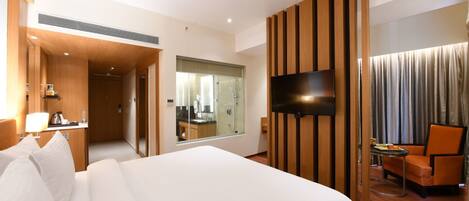 A hotel room with a large bed, a TV mounted on the wall, a desk with a lamp, and a chair.