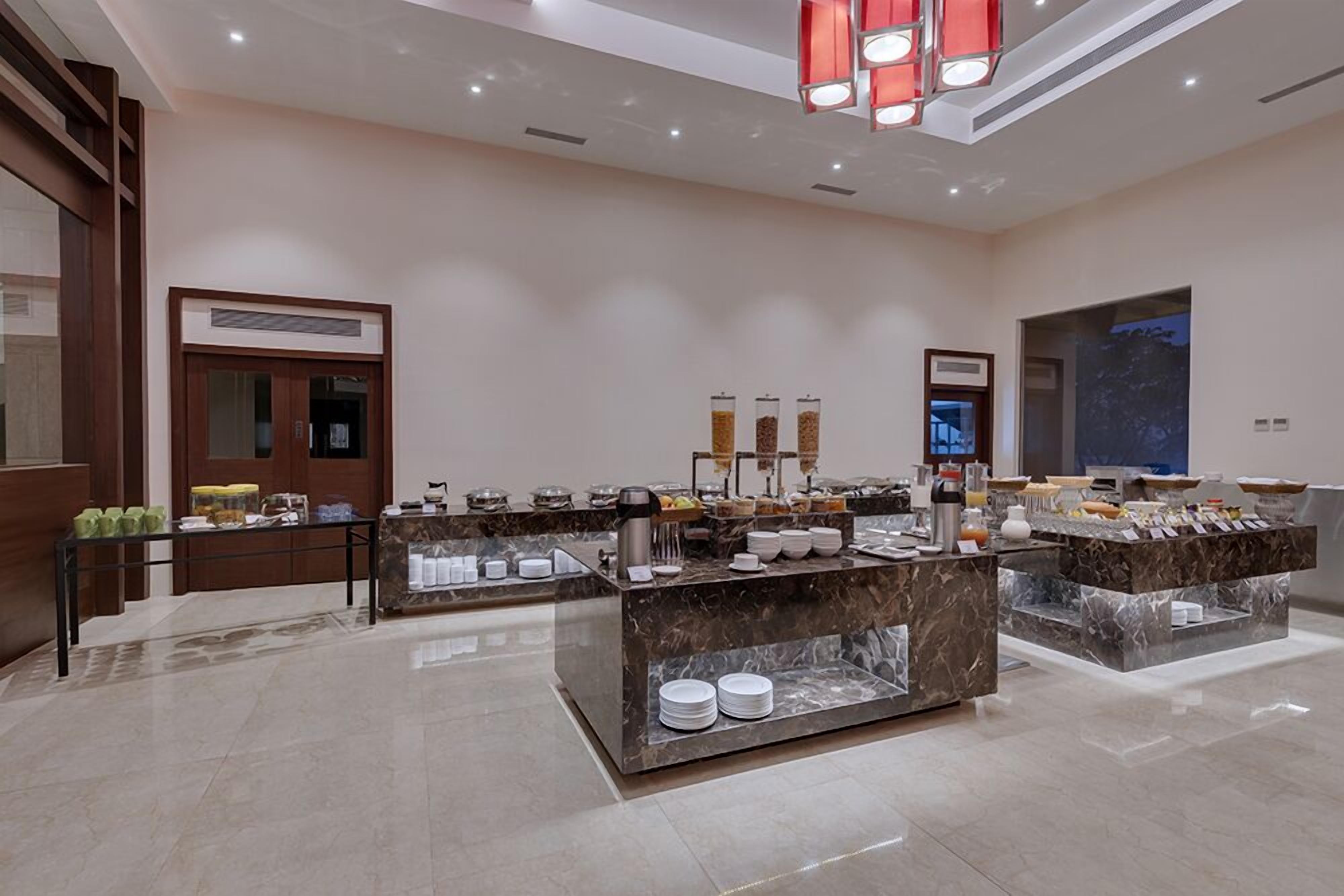 Un espace moderne pour le petit-déjeuner, dans un hôtel, avec des comptoirs en marbre, un coin café et un écran numérique.