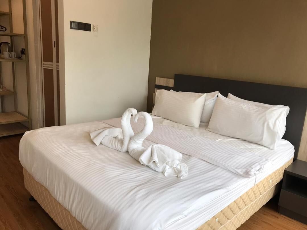 Un lit bien fait, agrémenté d’une serviette pliée en forme de cygne, d’une tête de lit en bois et d’une table de chevet.