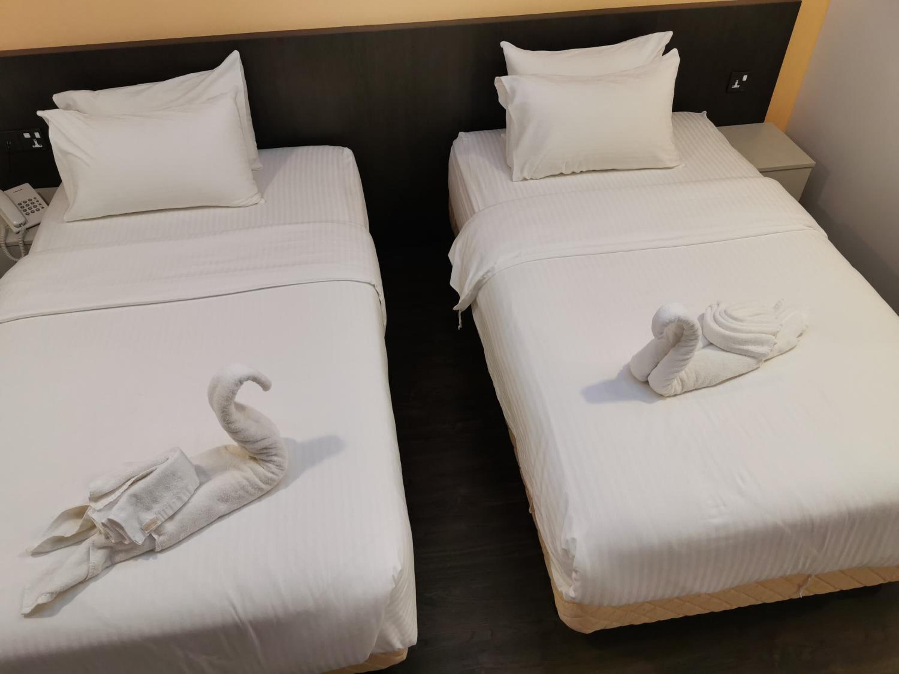 Duas camas de solteiro com lençóis e almofadas brancas, um telefone ao lado de cada cama e uma toalha dobrada em cada uma.