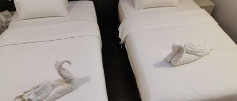 Duas camas de solteiro com lençóis e almofadas brancas, um telefone ao lado de cada cama e uma toalha dobrada em cada uma.