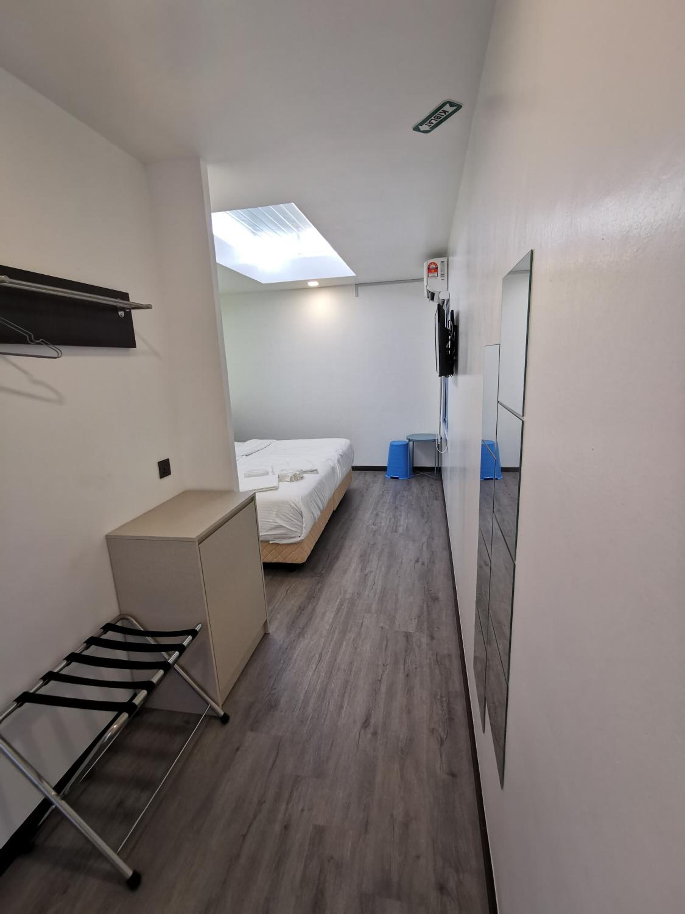 Una habitación de hotel compacta con una cama, un escritorio pequeño, un tendedero y una unidad de aire acondicionado instalada en el techo.