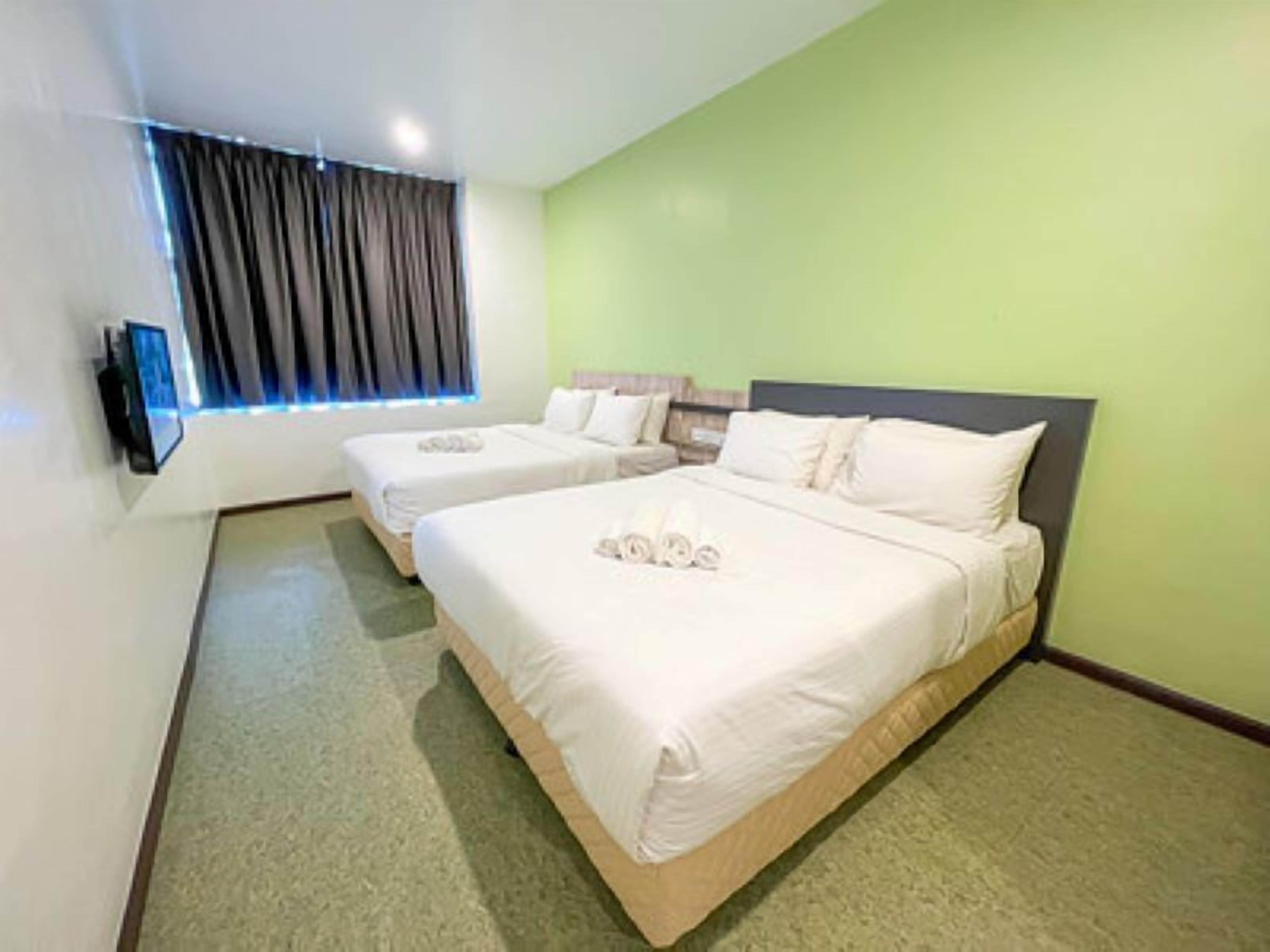Habitación de hotel con dos camas, un televisor de pantalla plana montado en la pared y una ventana con cortinas.