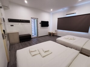 Habitación de hotel con dos camas, un escritorio, una silla, un televisor y un aire acondicionado.