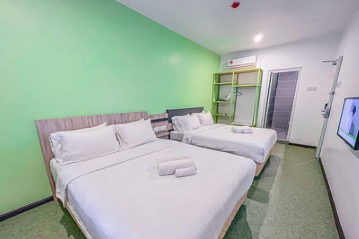 Ett hotellrum med två sängar, en grön vägg, en garderob och en tv som hänger på väggen.