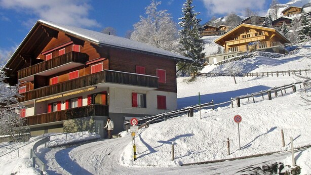 A wooden chalet with balconies, a ski lift, and a snow-covered mountain in the background. - Lovely apartment for 5 guests with WIFI and TV (Unter Eiger)