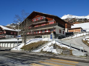 A multi-story hotel with balconies, a ski slope in the background, and a clear sky.