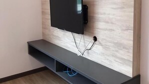 A modern wall-mounted TV with a wooden panel backdrop, a dark console below, and visible cables. - TT Dorf Hotel Matang (Taiping)