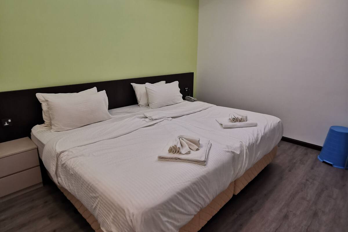 A modern hotel room with a skylight, a large bed with white linens, a bedside table, and a blue trash bin.