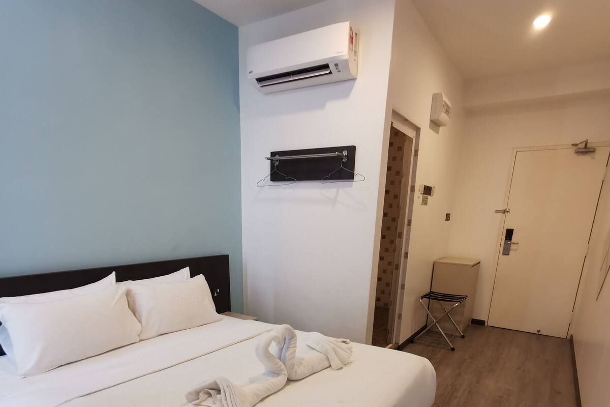A hotel room with a bed, a wall-mounted air conditioner, a door, and a small seating area.